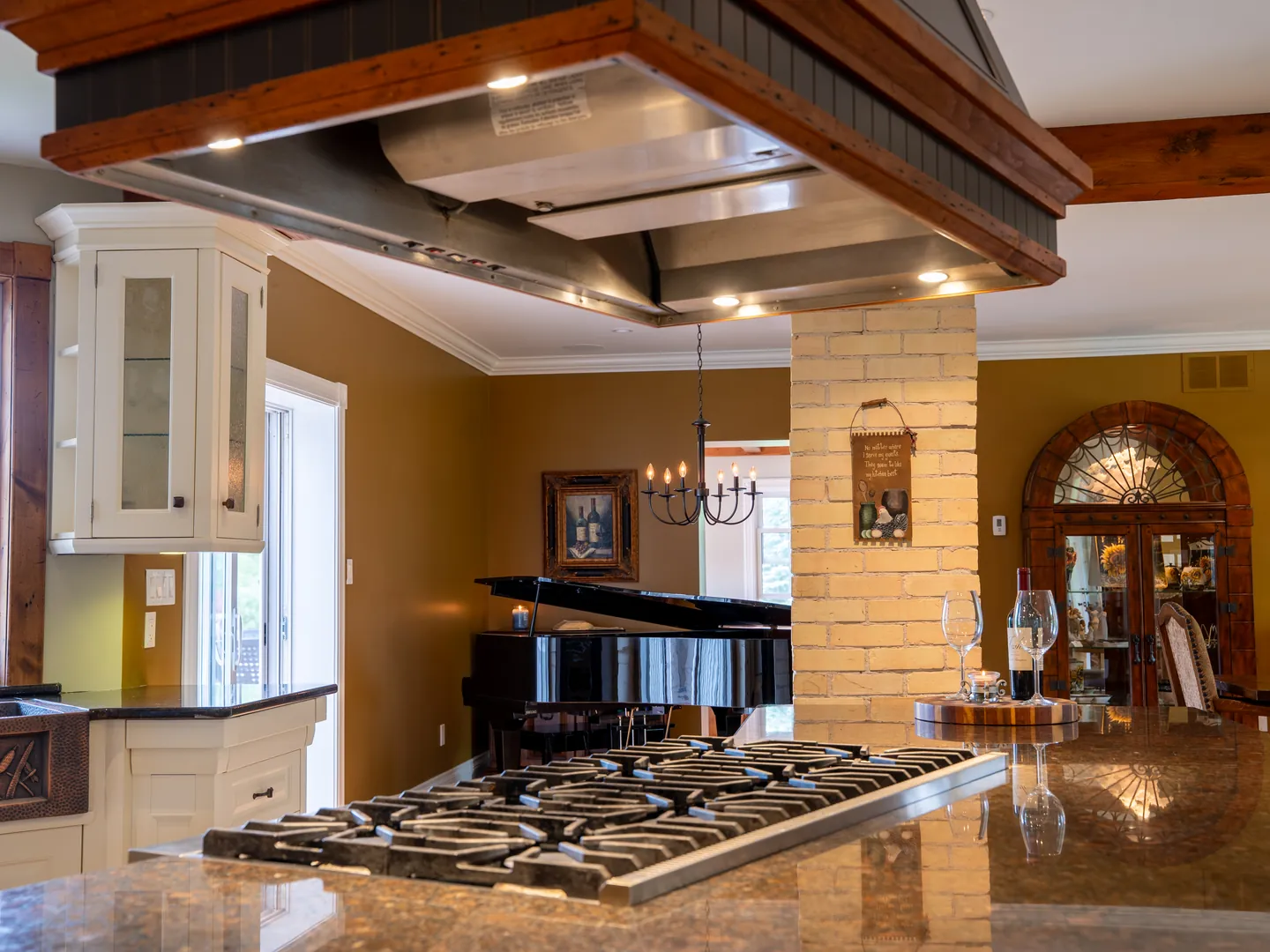 Range and hood beneath timber beams, beside a brick column and granite counter