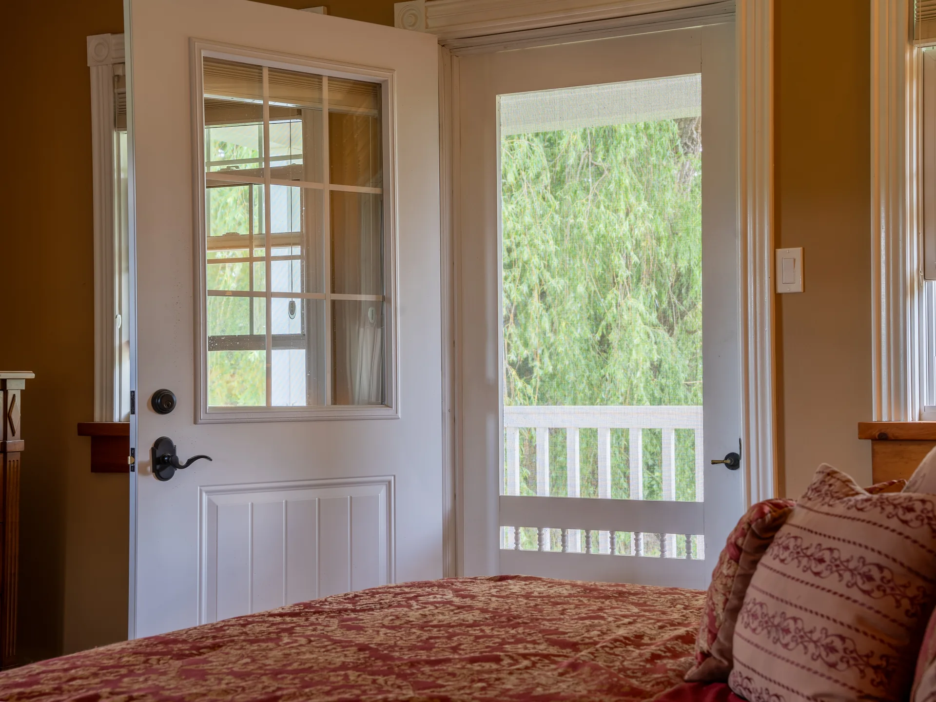 Bed pillows in the foreground beside the open French door to a screened porch.